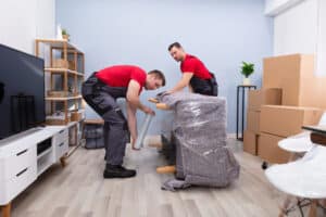Two Male Removalist Wrapping A Sofa